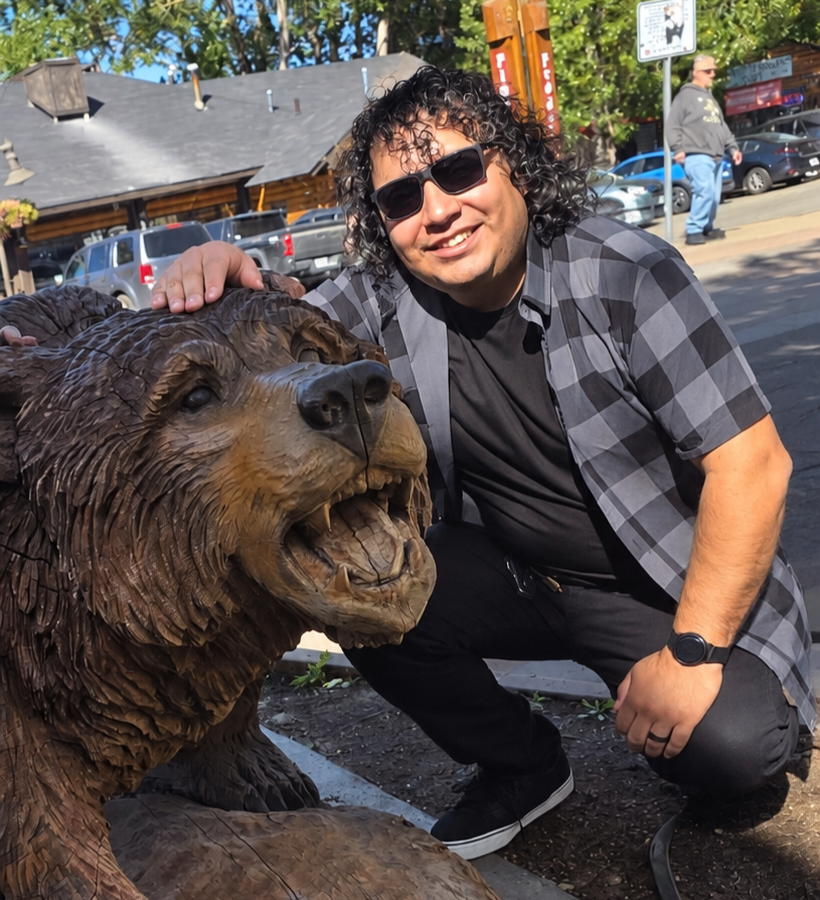 Person posing beside a wooden bear carving outdoors
